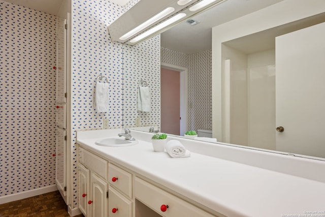 bathroom featuring visible vents, vanity, baseboards, and wallpapered walls