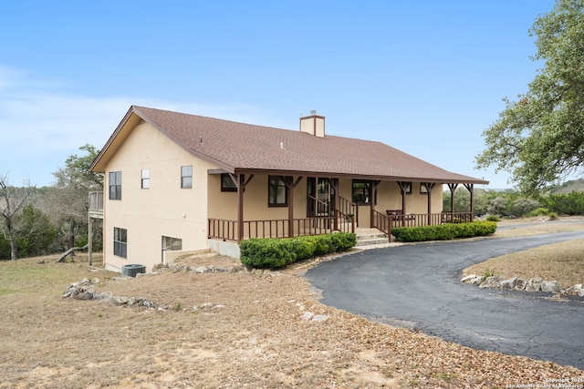 view of front facade with central AC unit, a chimney, aphalt driveway, covered porch, and stucco siding