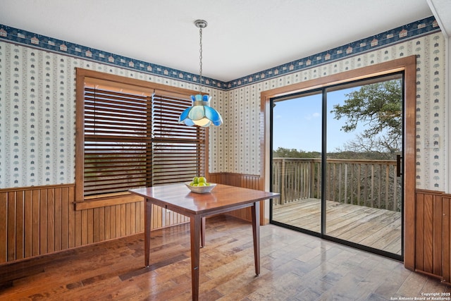 dining room with wallpapered walls, wood finished floors, and wainscoting