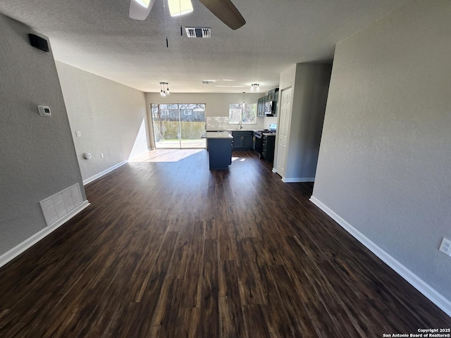 unfurnished living room with a ceiling fan, dark wood-style flooring, visible vents, and baseboards