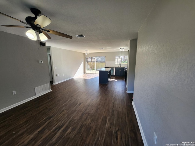 unfurnished living room with a sink, dark wood finished floors, visible vents, and baseboards