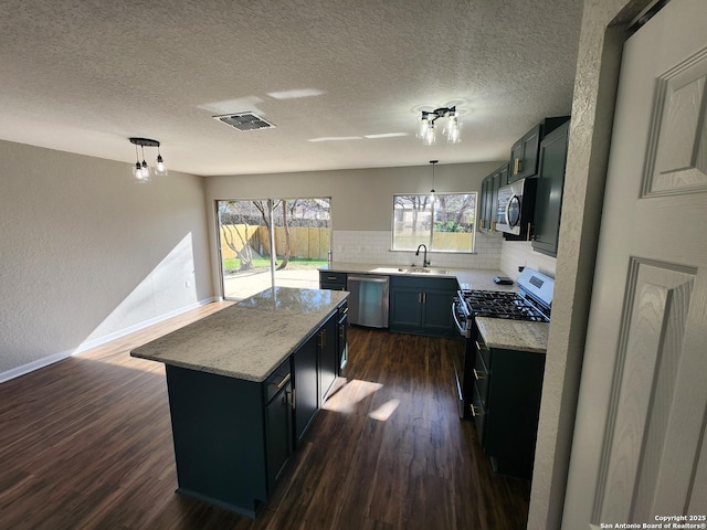 kitchen with stainless steel appliances, dark wood-style flooring, a sink, a kitchen island, and pendant lighting