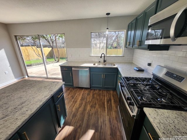 kitchen with light stone counters, pendant lighting, dark wood finished floors, stainless steel appliances, and a sink