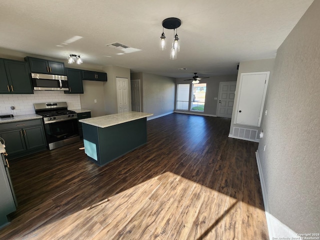 kitchen with stainless steel appliances, dark wood-type flooring, a kitchen island, light countertops, and decorative light fixtures