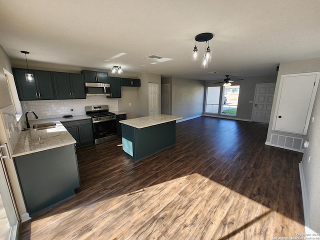 kitchen with light stone counters, decorative light fixtures, appliances with stainless steel finishes, a sink, and a kitchen island