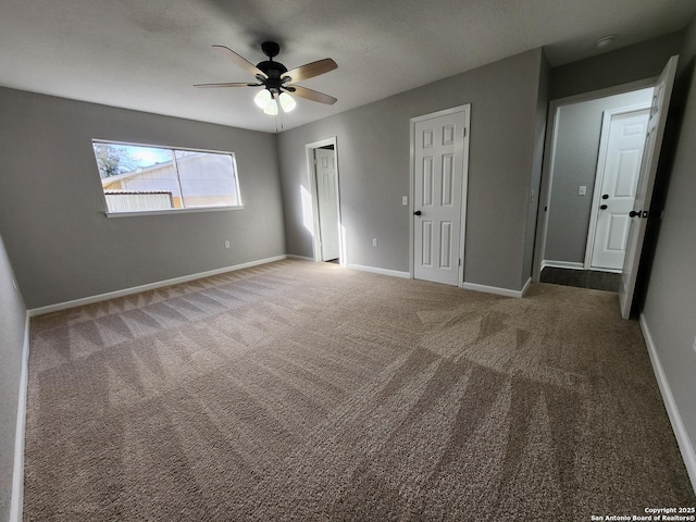 unfurnished bedroom featuring carpet, baseboards, ceiling fan, and two closets