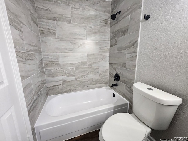 bathroom with shower / washtub combination, a textured wall, and toilet