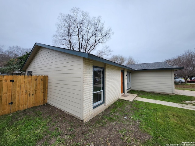 view of side of home with a yard, brick siding, and fence