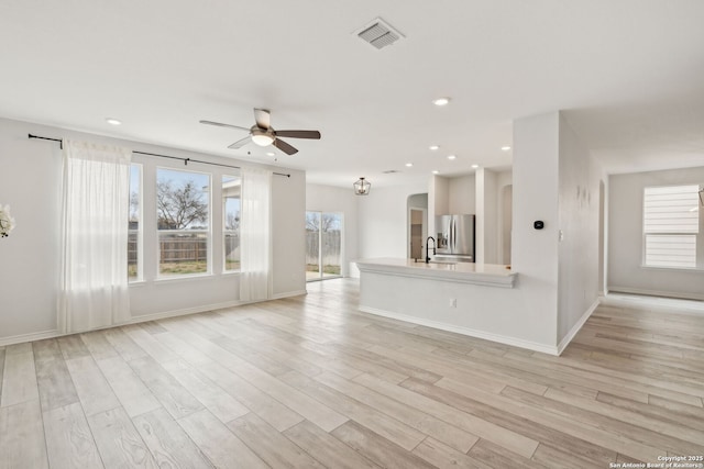 unfurnished living room with ceiling fan, arched walkways, light wood-style flooring, a sink, and visible vents