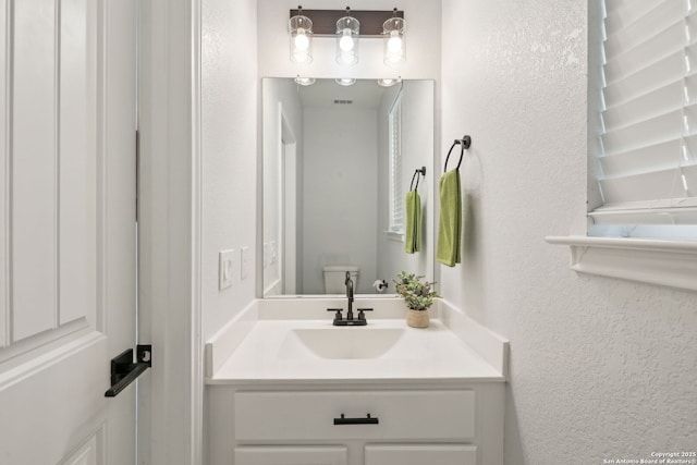 bathroom featuring a textured wall, vanity, and toilet