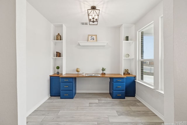 unfurnished office with visible vents, built in study area, light wood-style flooring, and baseboards