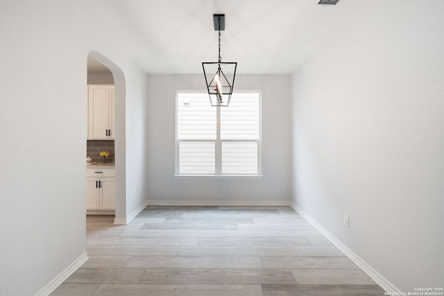 unfurnished dining area featuring light wood finished floors, visible vents, baseboards, and arched walkways