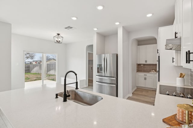 kitchen with stainless steel refrigerator with ice dispenser, visible vents, white cabinetry, a sink, and black electric cooktop