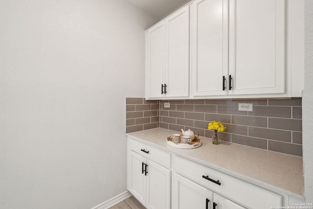 interior space featuring tasteful backsplash, white cabinetry, light countertops, and baseboards