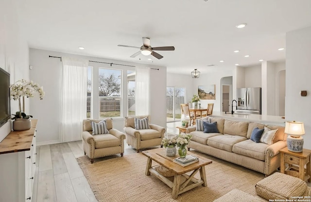 living area with arched walkways, recessed lighting, light wood-style flooring, a ceiling fan, and baseboards