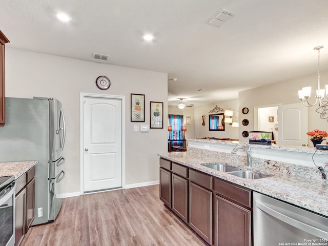 kitchen with sink, light stone counters, hanging light fixtures, stainless steel appliances, and light hardwood / wood-style floors