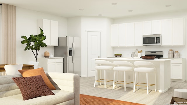 kitchen with a breakfast bar, appliances with stainless steel finishes, white cabinetry, a center island with sink, and light wood-type flooring