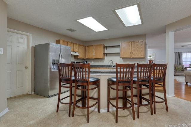 kitchen featuring stainless steel fridge, light brown cabinets, a textured ceiling, and a kitchen bar