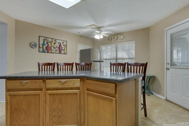 kitchen with a textured ceiling, stainless steel refrigerator, a kitchen breakfast bar, a kitchen island, and ceiling fan