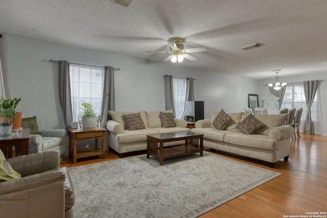 living room with wood-type flooring, ceiling fan with notable chandelier, and a textured ceiling