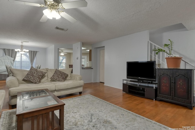 living room with ceiling fan with notable chandelier, hardwood / wood-style floors, and a textured ceiling