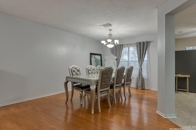 dining room featuring an inviting chandelier, light hardwood / wood-style flooring, and a textured ceiling