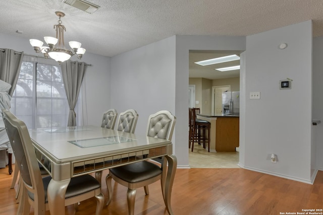 dining area featuring a chandelier, a textured ceiling, and light wood-type flooring