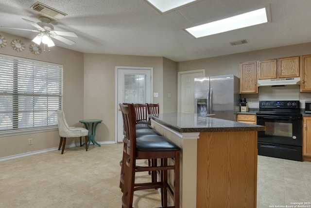 kitchen featuring stainless steel fridge, ceiling fan, a kitchen breakfast bar, a center island, and black electric range