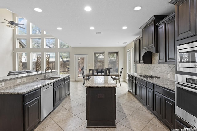 kitchen with an island with sink, sink, backsplash, light stone counters, and stainless steel appliances