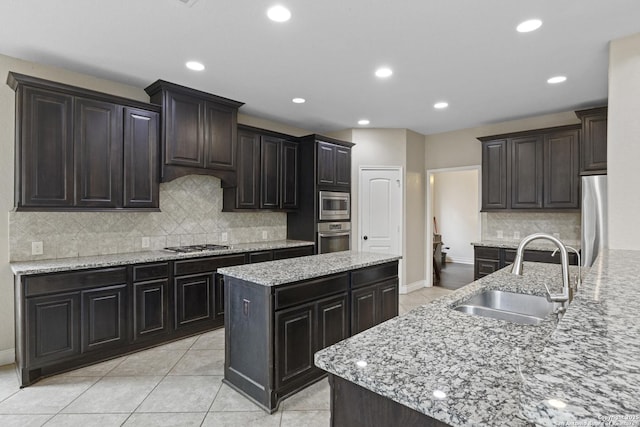 kitchen with a kitchen island with sink, sink, light tile patterned flooring, and appliances with stainless steel finishes