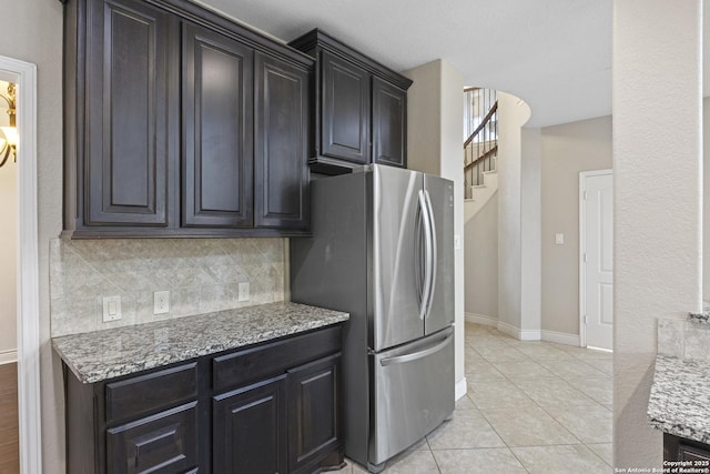 kitchen with light stone countertops, light tile patterned floors, stainless steel fridge, and decorative backsplash