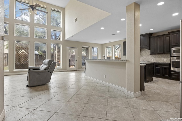 kitchen featuring light stone counters, light tile patterned floors, appliances with stainless steel finishes, ceiling fan, and decorative backsplash