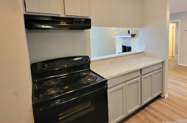 kitchen with black range with electric stovetop, light hardwood / wood-style flooring, and light stone countertops