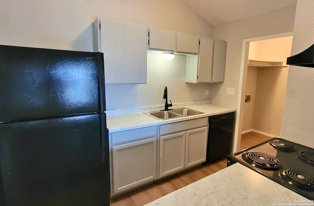 kitchen featuring vaulted ceiling, white cabinetry, sink, black appliances, and light hardwood / wood-style flooring