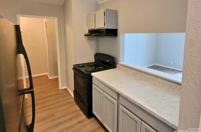 kitchen featuring black / electric stove, stainless steel fridge, light stone countertops, and light hardwood / wood-style flooring