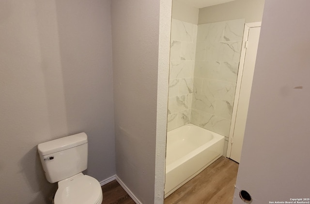 bathroom featuring wood-type flooring, tiled shower / bath, and toilet