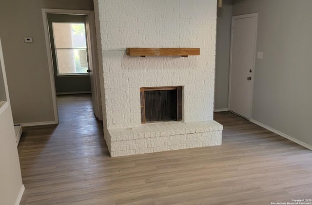 unfurnished living room featuring a baseboard radiator, a brick fireplace, and hardwood / wood-style floors