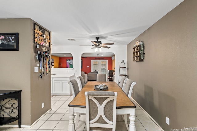 dining room featuring arched walkways, light tile patterned floors, visible vents, baseboards, and a ceiling fan