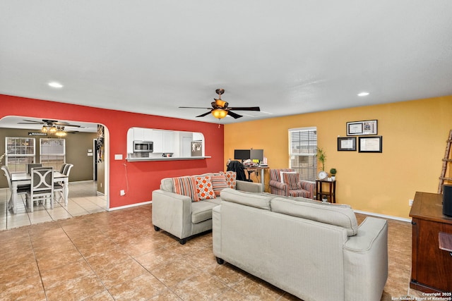 living area featuring light tile patterned floors, baseboards, arched walkways, and a ceiling fan