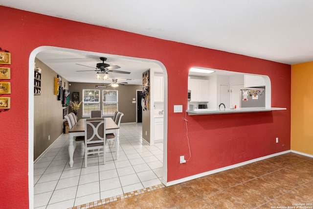 dining room with arched walkways, tile patterned flooring, a ceiling fan, and baseboards