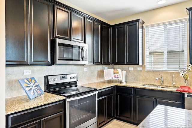 kitchen featuring light tile patterned flooring, appliances with stainless steel finishes, tasteful backsplash, sink, and light stone counters