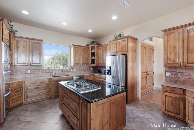 kitchen with sink, a center island, dark stone countertops, stainless steel appliances, and decorative backsplash