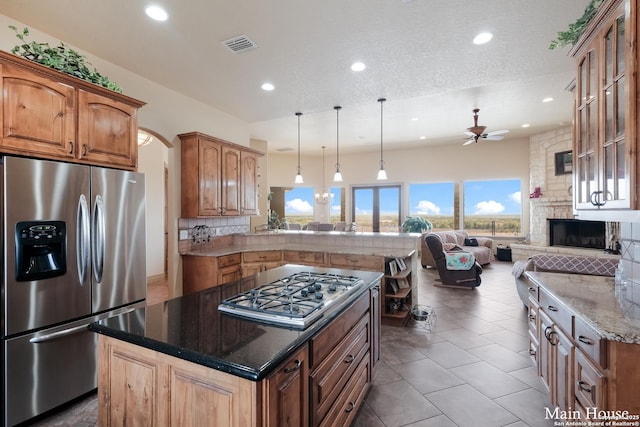 kitchen featuring appliances with stainless steel finishes, a fireplace, decorative light fixtures, dark stone countertops, and decorative backsplash