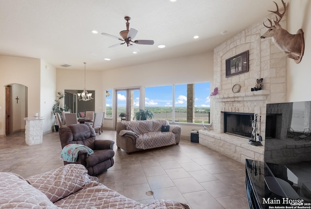 tiled living room featuring a stone fireplace and ceiling fan with notable chandelier