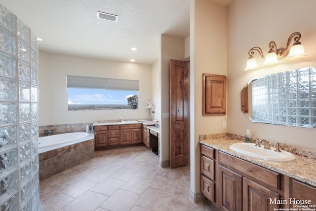 bathroom with a relaxing tiled tub, tile patterned floors, vanity, and a textured ceiling