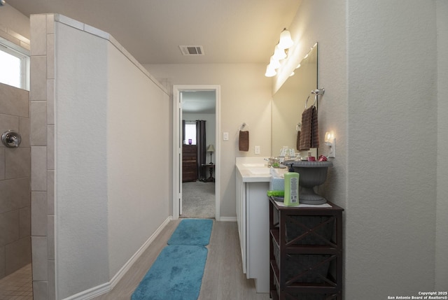 bathroom with tiled shower, vanity, and hardwood / wood-style floors