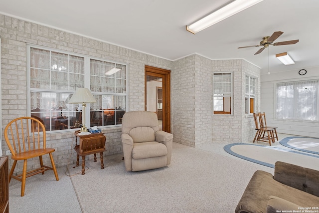 carpeted living room featuring ceiling fan and brick wall