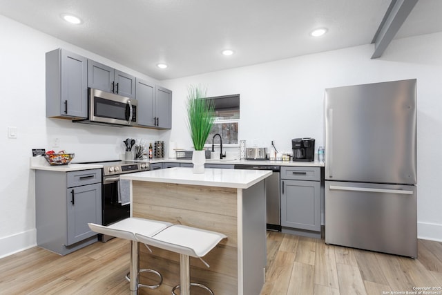 kitchen featuring appliances with stainless steel finishes, gray cabinets, light hardwood / wood-style floors, and a kitchen island