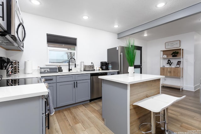 kitchen featuring sink, light hardwood / wood-style flooring, appliances with stainless steel finishes, a kitchen island, and a kitchen bar