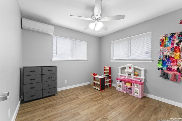 rec room with ceiling fan, a wall mounted AC, and light wood-type flooring